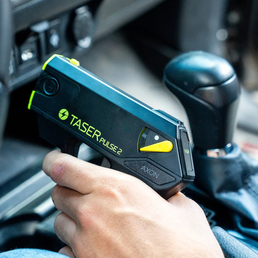 Hand holding a TASER Pulse 2 Reloadable Shooting Stun Gun inside a car
