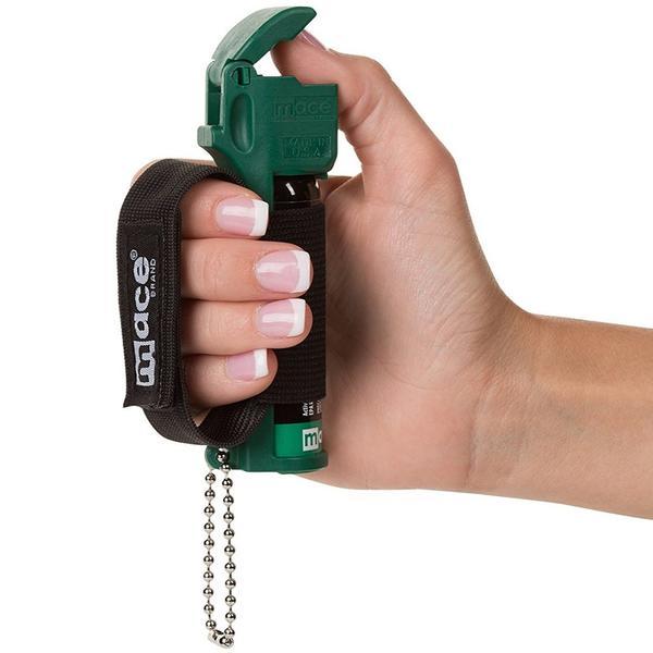 A hand holding a 14g Mace Muzzle Dog Repellent Jogger Pepper Spray in a handstrap