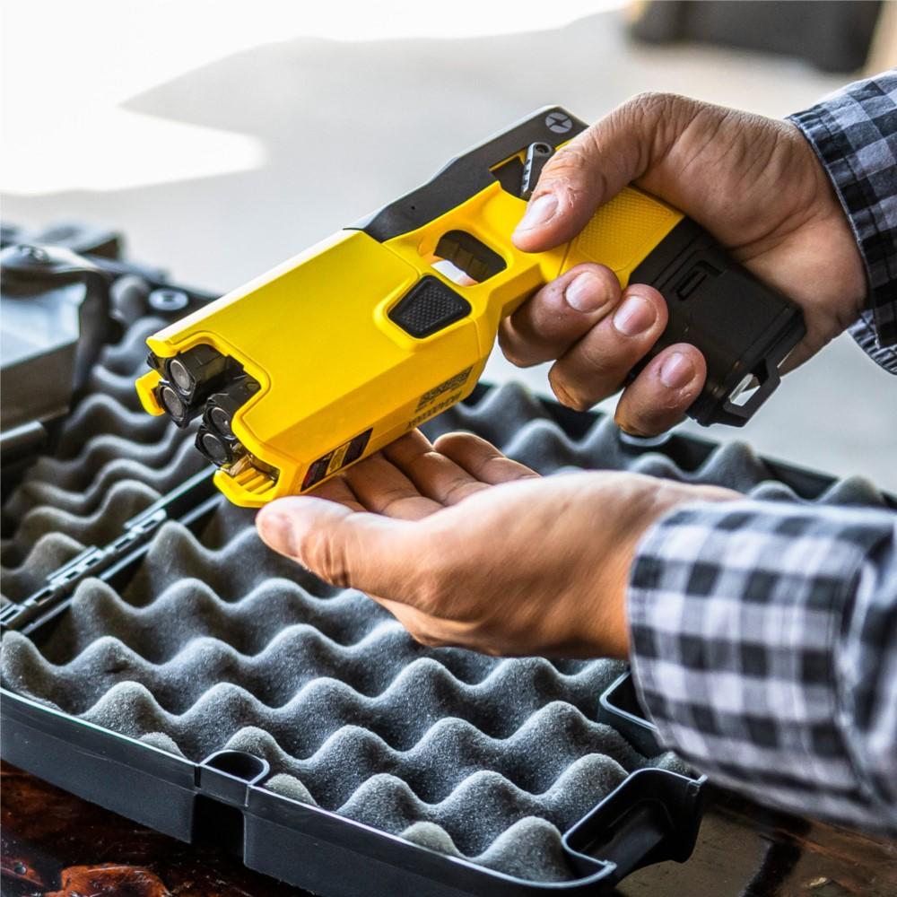 A person holding a TASER 7 CQ Home Defense Shooting Stun Gun over an open hard carrying case