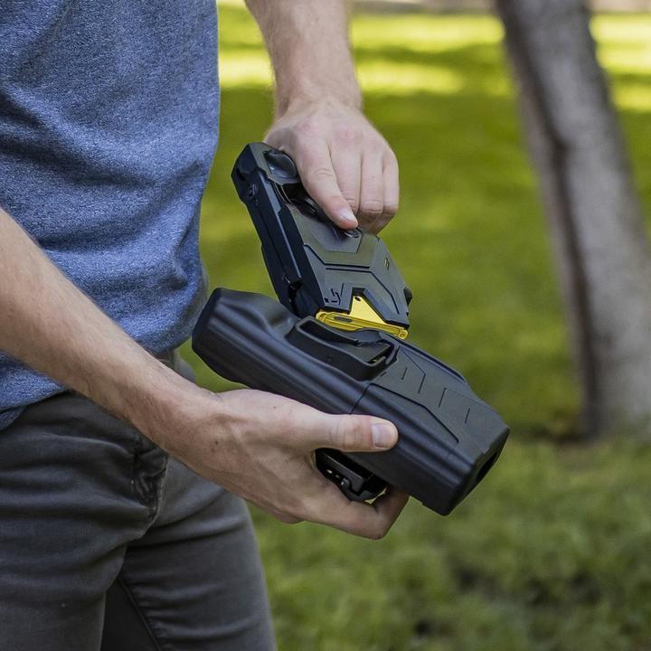 Hands placing a BLACKHAWK! TASER X2 into a Quick Draw Holster