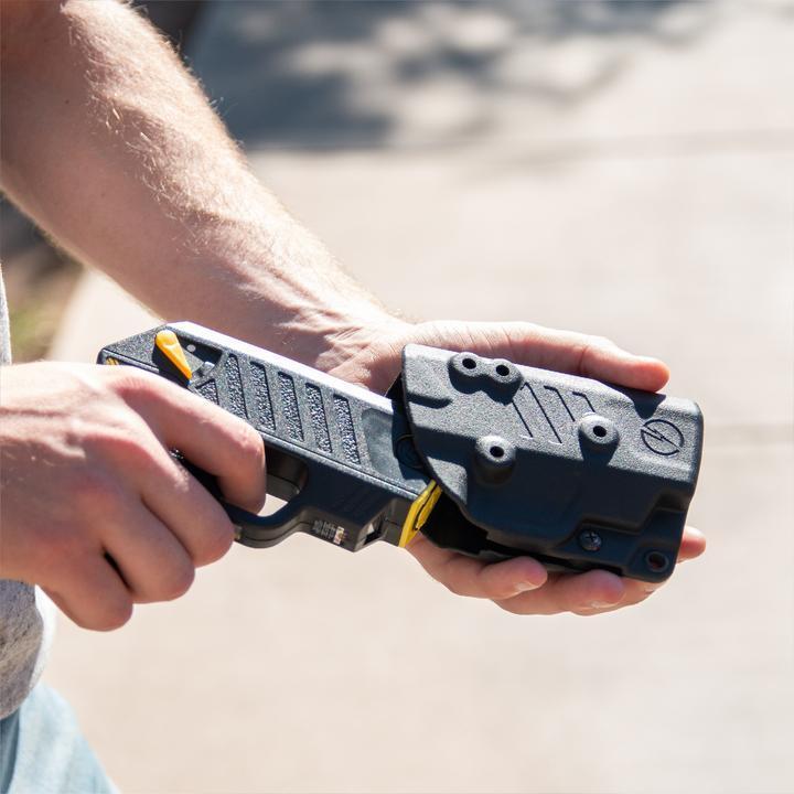 Hands securing a black TASER Pulse into its fitted Kydex holster