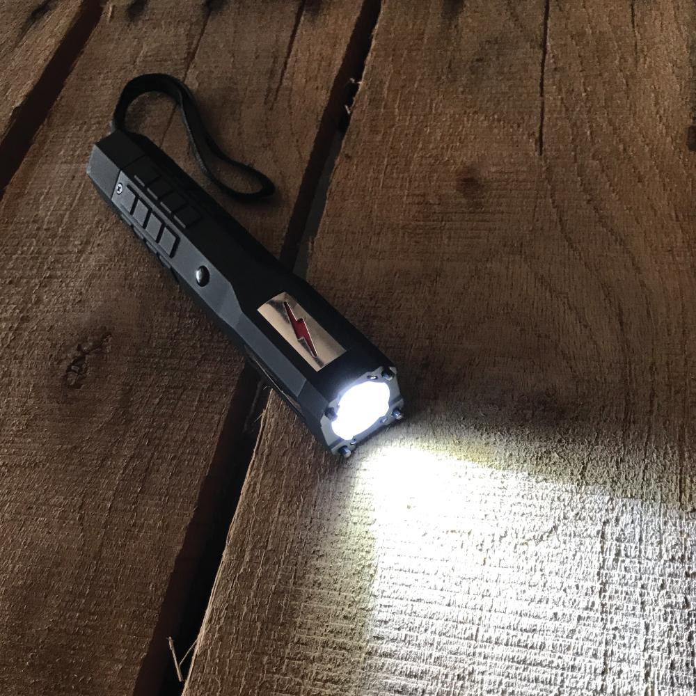 JOLT Lightning Rod Stun with Flashlight on with wrist strap lying on a wooden surface