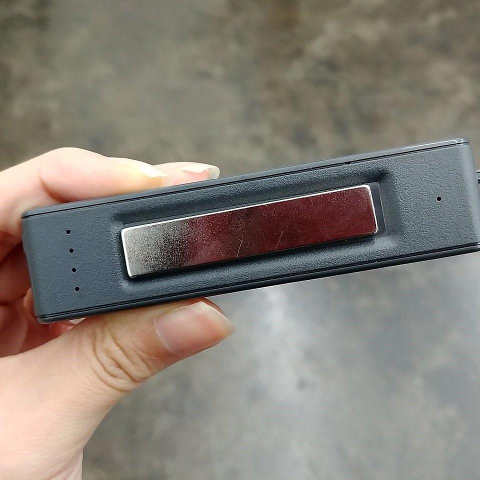 Hand holding the black 150-Day voice recorder and power bank, showing the built-in magnetic mount strip and battery indicator lights