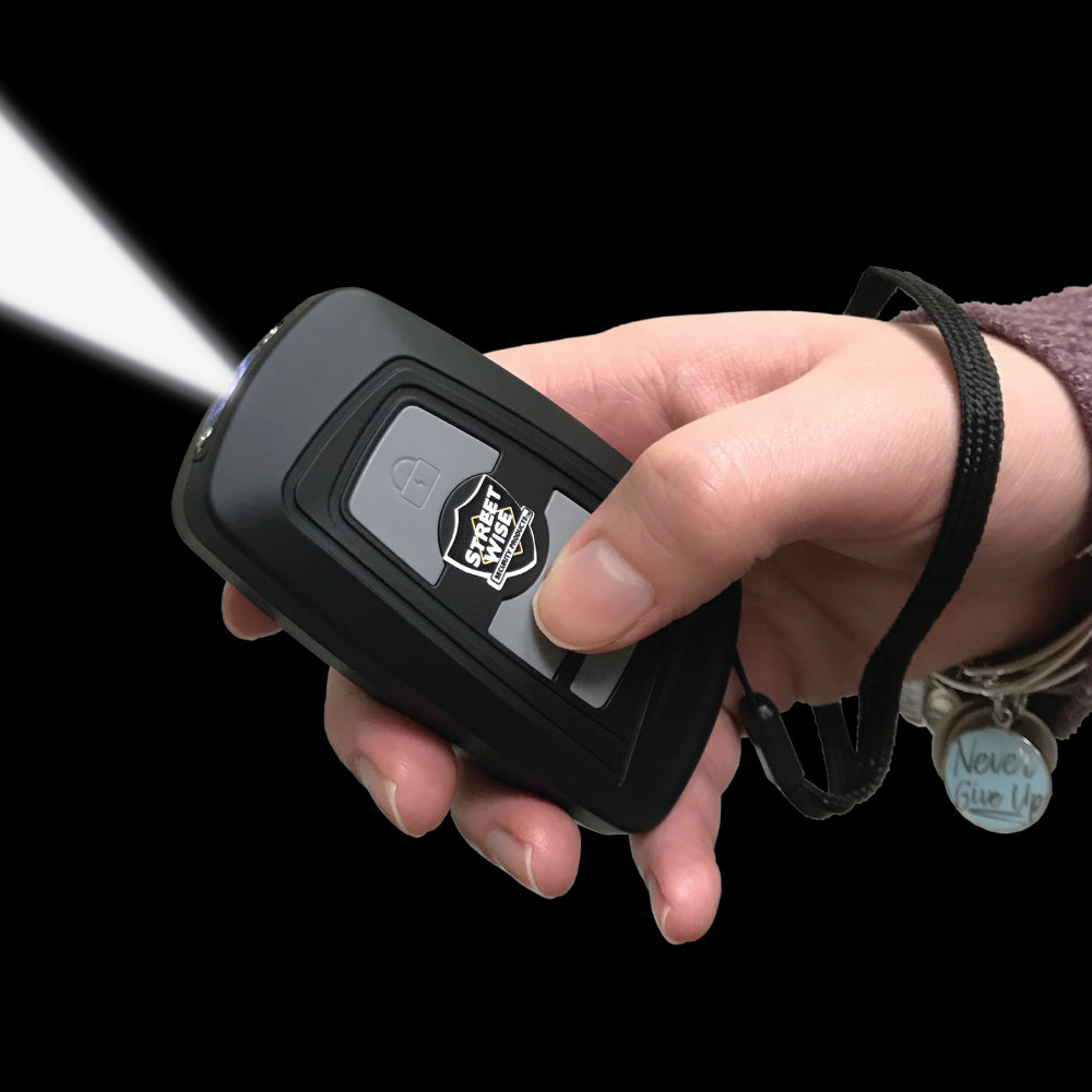 Black Fake Key Fob Mini Stun Gun Panic Alarm with silver buttons and wrist strap in hand