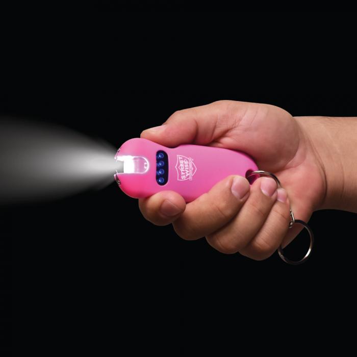 A hand holding a Pink stun gun from Streetwise with flashlight on in a dark setting