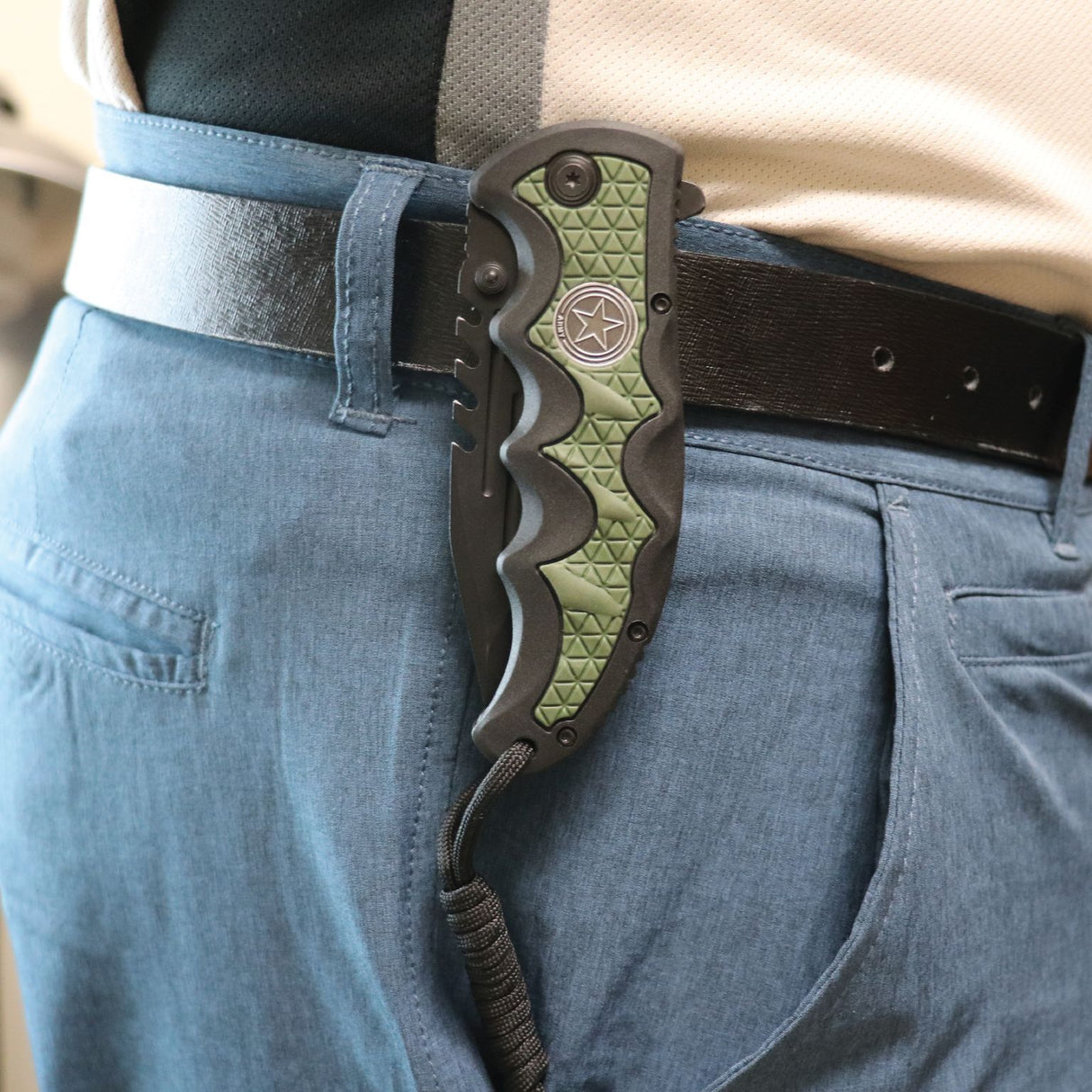 a folded Black 3.5" tactical knife by Elite Edge with an army green camouflage handle with paracord clipped to a person's belt