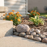 Decorative garden with fake key holder rocks, flowers, and plants in front of a house.