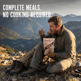 Man eating a meal from a backpack in a mountainous area with text 'Complete meals. No cooking required.'