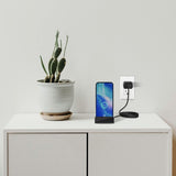 SpyWfi Hidden Motion Detection Spy Camera disguised as a phone charging dock, sits on a white cabinet next to a plant, plugged into a wall outlet