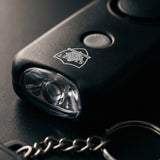 Close-up of a black keychain alarm with a flashlight attachment on a dark surface.