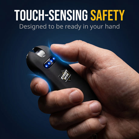 Hand holding a black touch-sensing safety device with text on a dark background