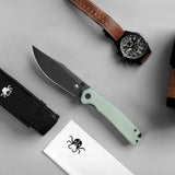 A fixed-blade knife with a matte black blade and a pale mint green handle is arranged on a light gray surface alongside a black nylon sheath, a white microfiber cloth, and a brown leather watch strap with a black chronograph watch.