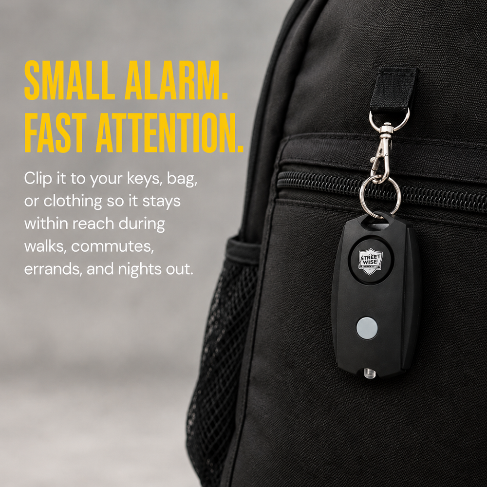 Close-up of the panic alarm clipped to a bag strap or keyring, with the compact black body clearly visible.