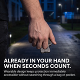 A close-up of a person's hand holding a small rectangular wearable safety device on a blurred nighttime outdoor path. Large text at the bottom reads, 'ALREADY IN YOUR HAND WHEN SECONDS COUNT.