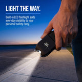 Streetwise Tap Out stun gun with built-in LED flashlight illuminating a sidewalk at dusk
