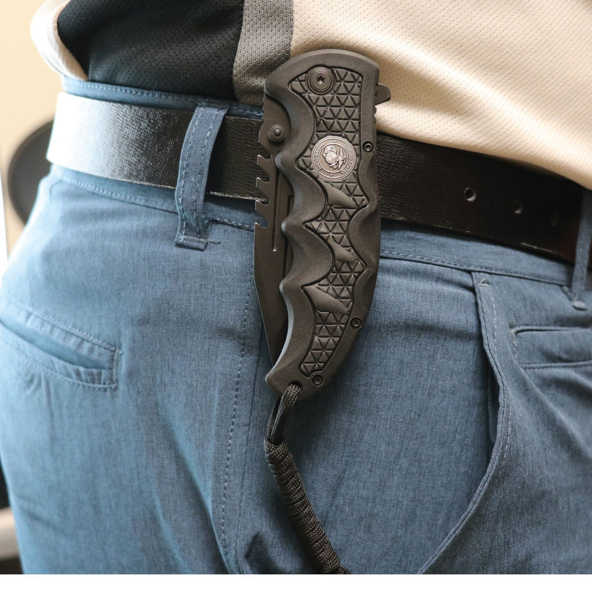 A closed Black 3.5" folding stainless steel pocket knife with paracord by Elite Edge clipped to a person's belt