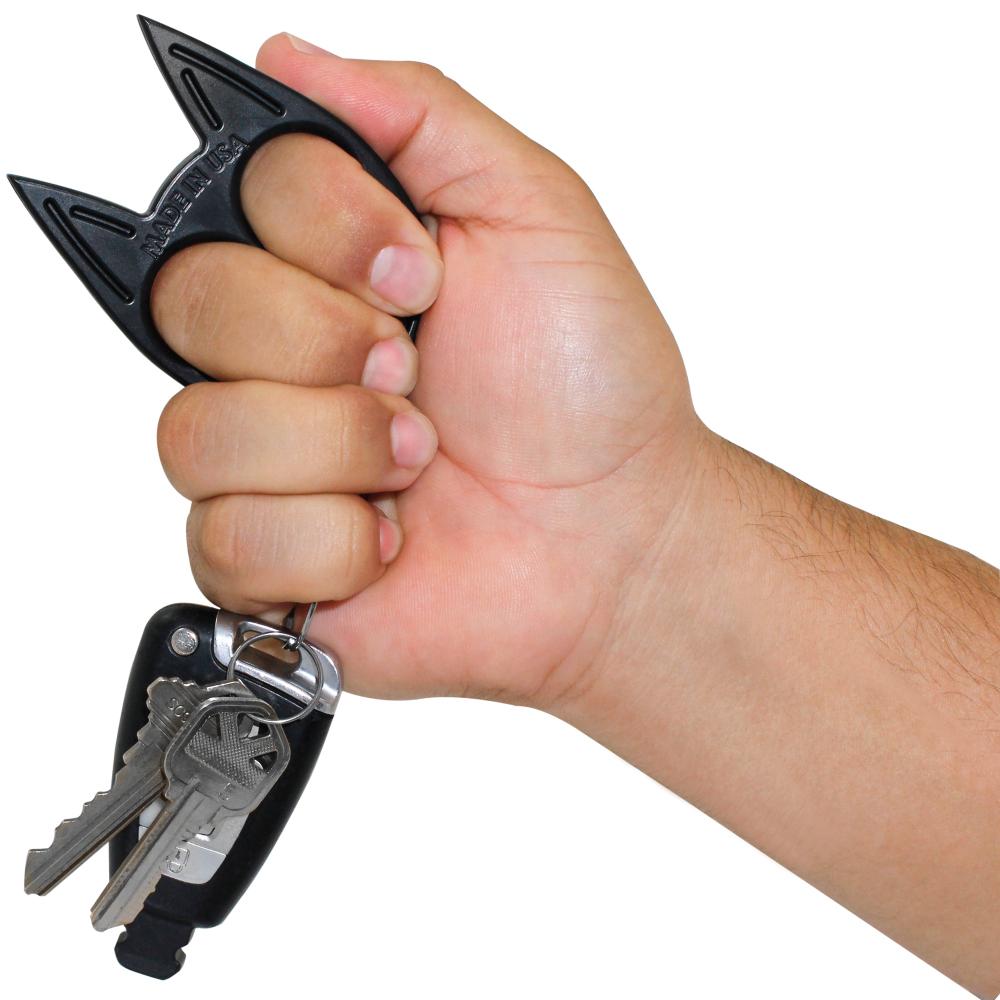 a hand gripping a Kitty knuckle self defense weapon that is part of the Stun Gun & Pepper Spray Self-Defense Keychain Weapon Set
