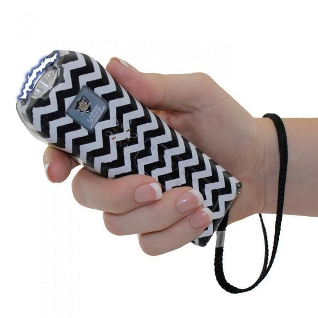 a hand holding Streetwise™ Ladies' Choice LED Stun Gun Alarm 21M with a black and white chevron pattern. It features a squeeze-n-stun button, an LED light, and a wrist strap for easy carrying.