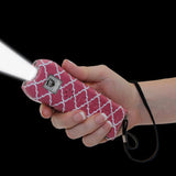 a hand holding a pink and white patterned Streetwise™ Ladies' Choice LED Stun Gun Alarm 21M with its flashlight on.