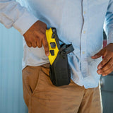 a man placing a TASER 7 CQ Home Defense Shooting Stun Gun into a black holster clipped to his pants.