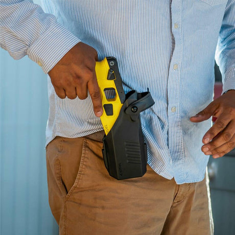 a man placing a TASER 7 CQ Home Defense Shooting Stun Gun into a black holster clipped to his pants.