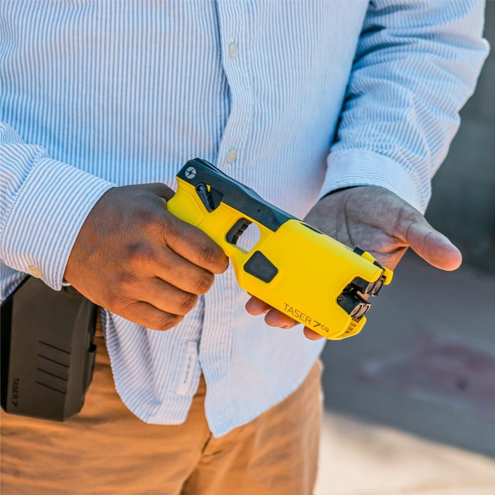 A person holding a TASER 7 CQ Home Defense Shooting Stun Gun in their hands, with the holster visible on their belt