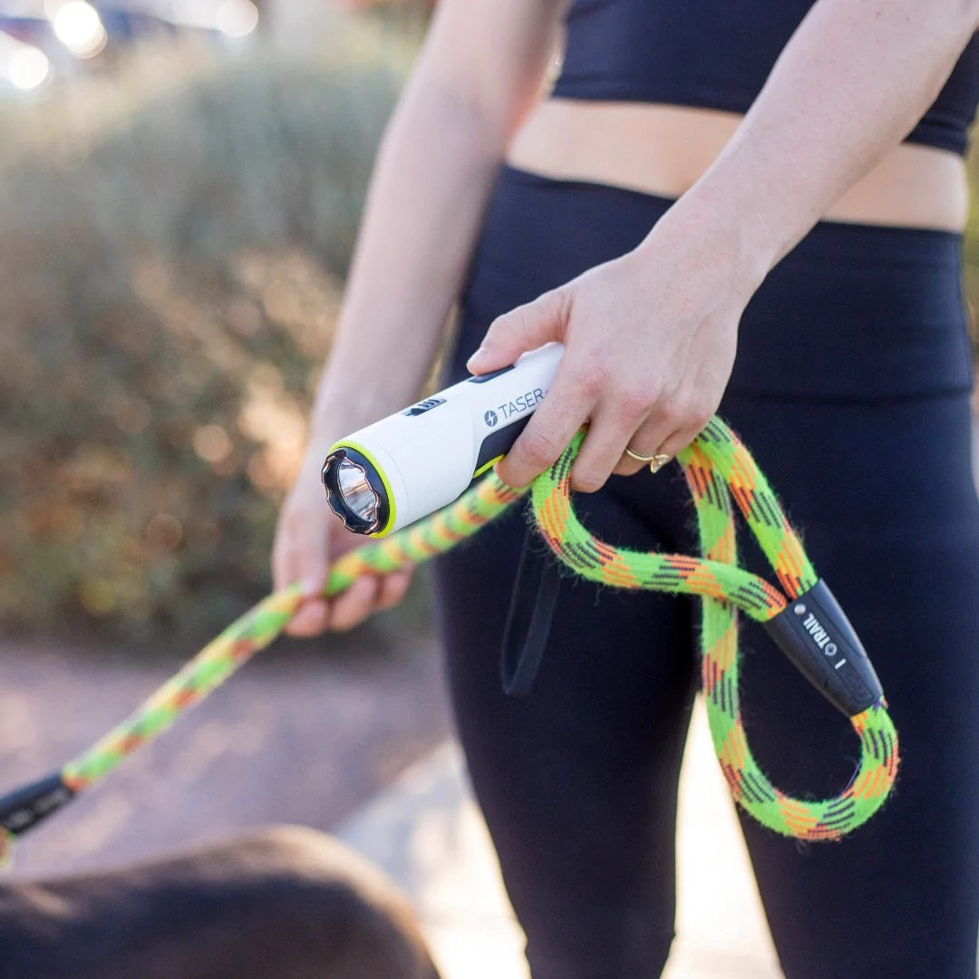 a hand holding a  white TASER Strikelight 2 Rechargeable Stun Gun Flashlight along with a dog leash