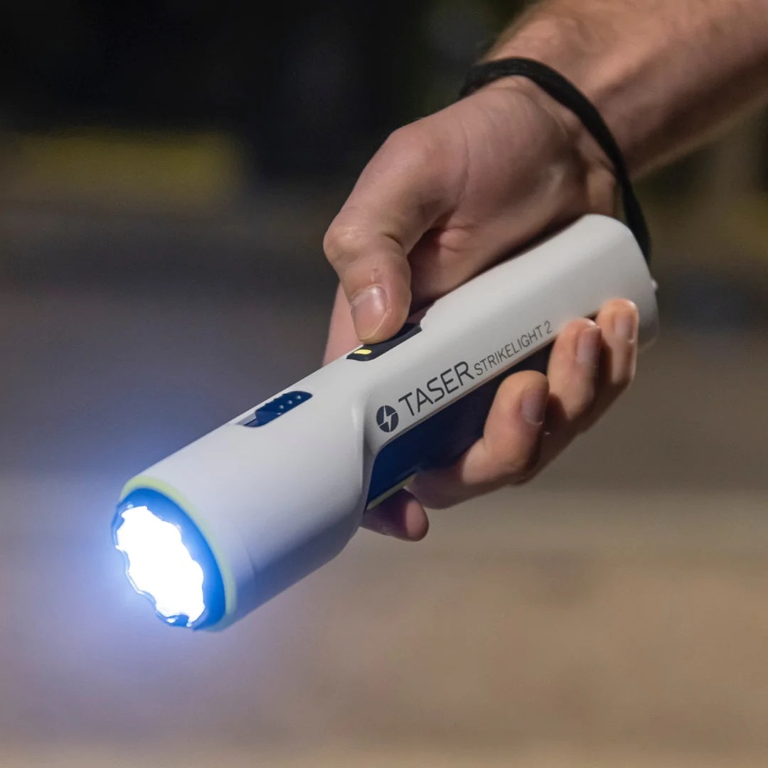 a hand holding a white TASER Strikelight 2 Rechargeable Stun Gun with the flashlight on.