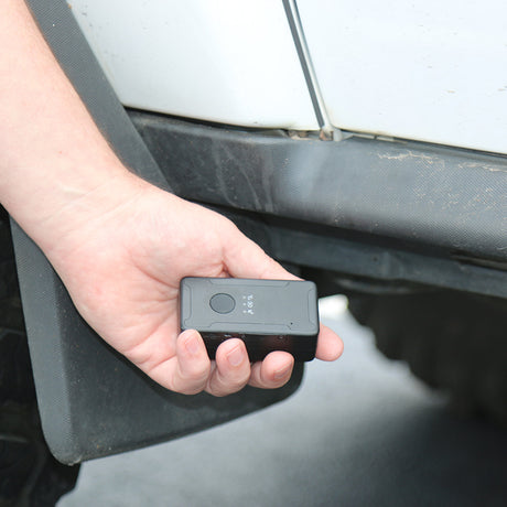 A hand holding and placing the iTrail Solo Mini Rechargeable 4G GPS Tracker under the car
